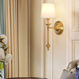 Brass wall sconce with fabric shade beside a mirror
