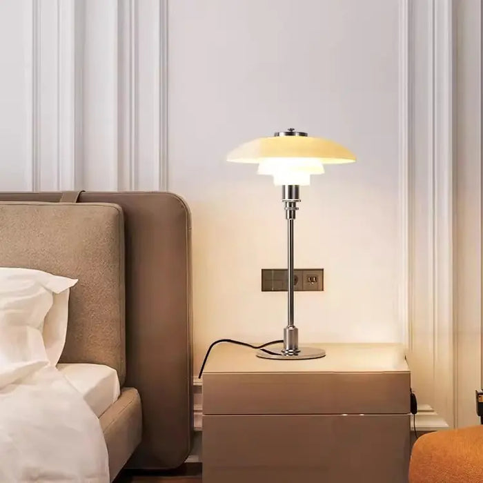 PH tiered lamp lit beside a bed