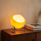 Handmade amber glass globe table lamp on a chrome cradle glowing on a walnut sideboard