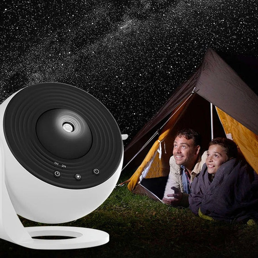 Father and child looking at a starry sky from a tent with the galaxy projector beside them