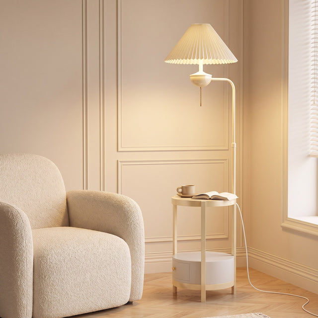 Cream floor lamp with pleated shade and built-in round side table beside a boucle armchair