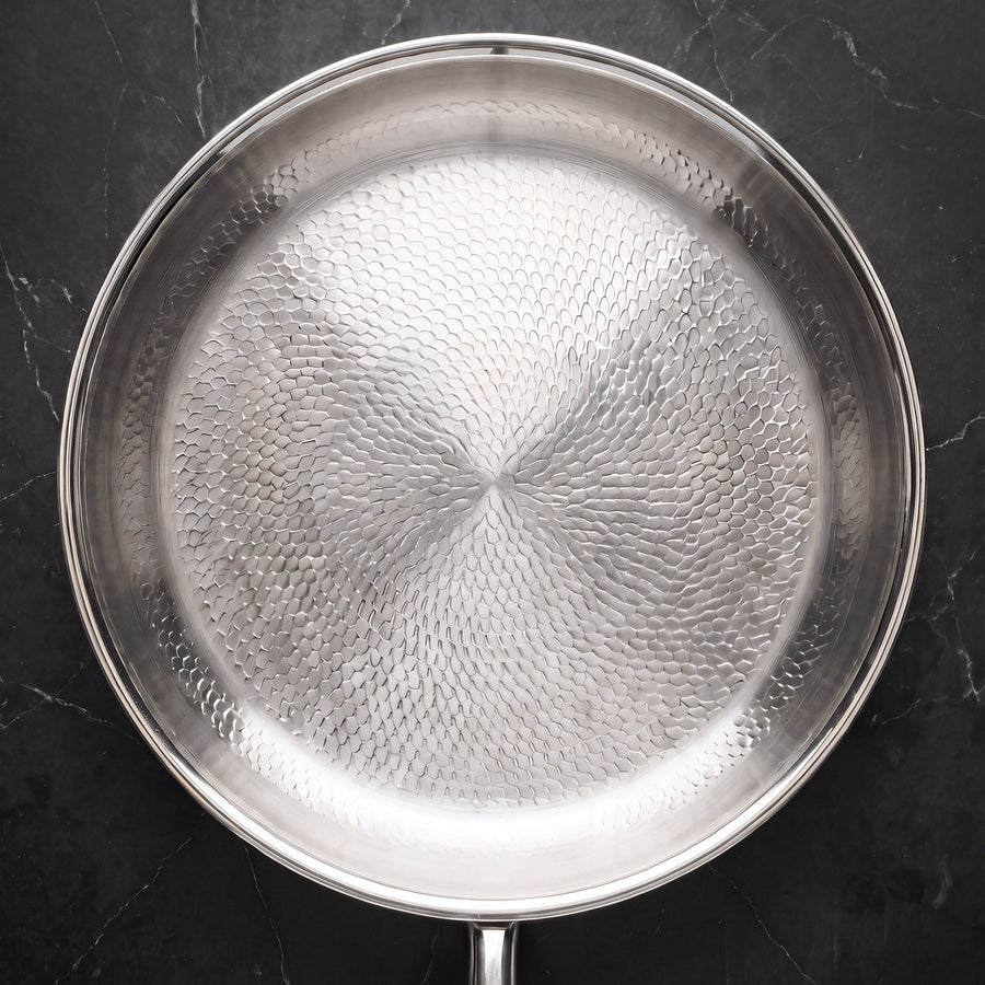 Overhead view of the titanium frying pan on a black marble counter, showing the hammered fish-scale cooking surface