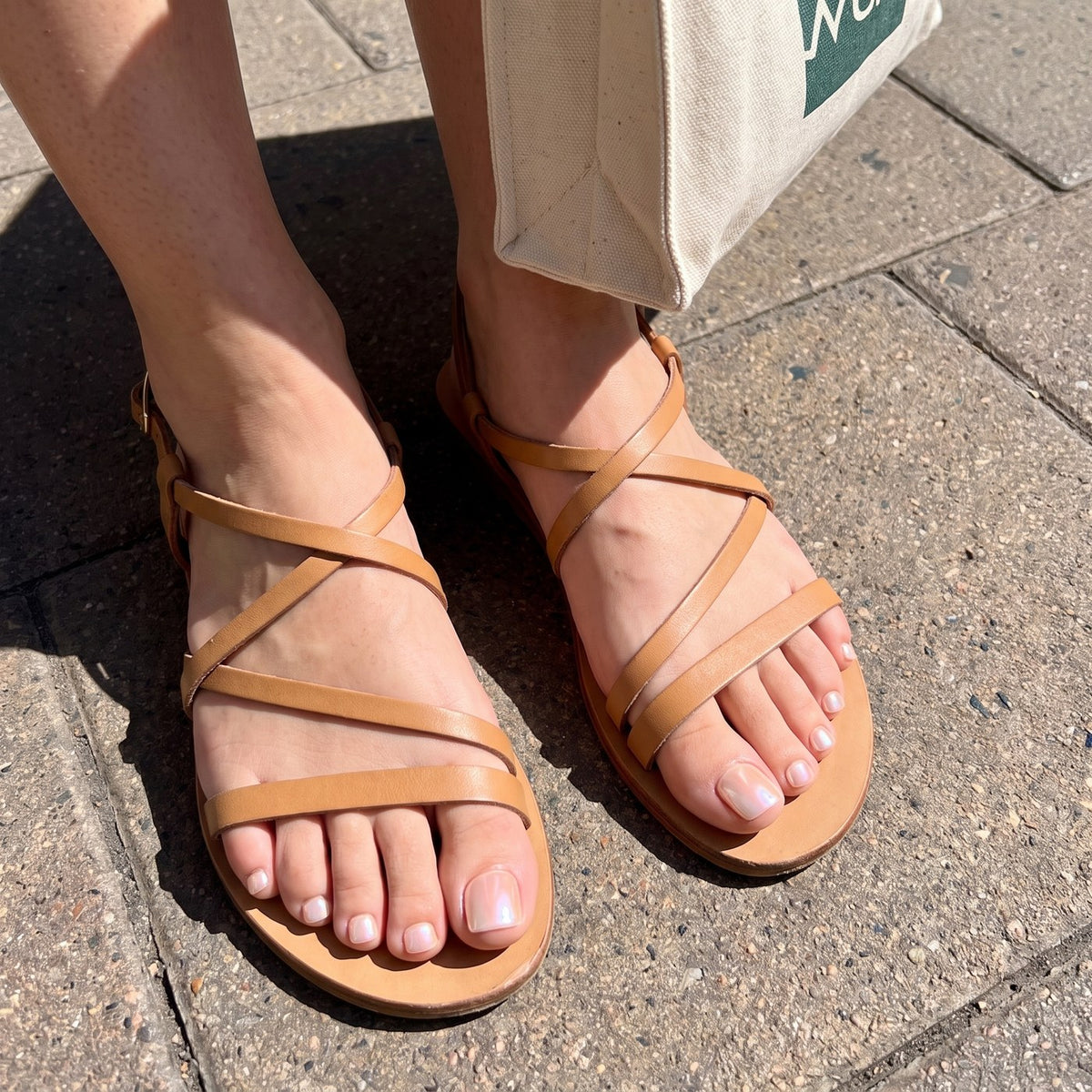 Pearl-chrome toenails on show in open tan sandals on a sunlit pavement