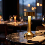 Wireless cordless rechargeable LED table lamp in brushed gold glowing on a dark marble dining table